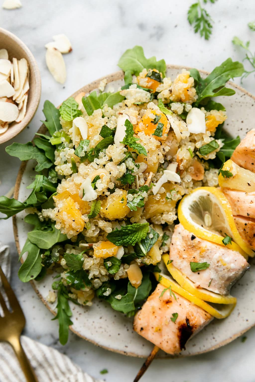 Serving of herbed quinoa pilaf with apricots and almonds on plate with grilled salmon kabobs.
