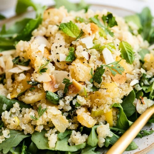 Close up view herbed quinoa pilaf served over arugula with apricots and almonds.