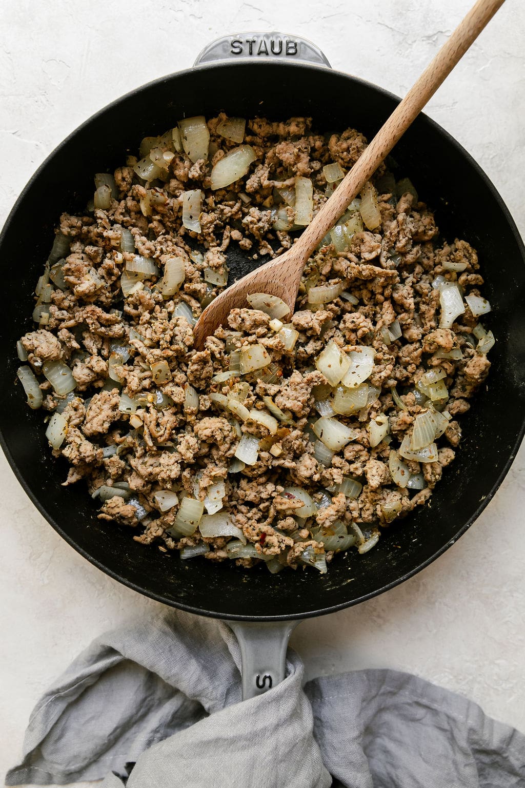 Browned turkey with garlic and yellow onion in Staub skillet with wooden spoon.
