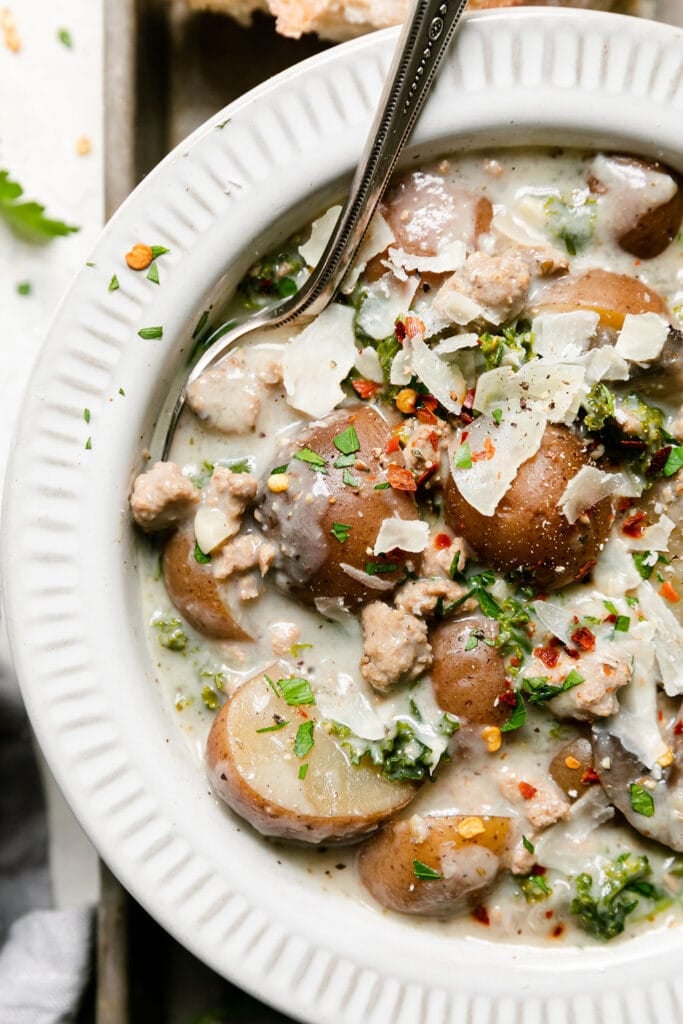 Close up overhead view zuppa toscana soup in white bowl on silver baking sheet topped with shaved Parmesan.