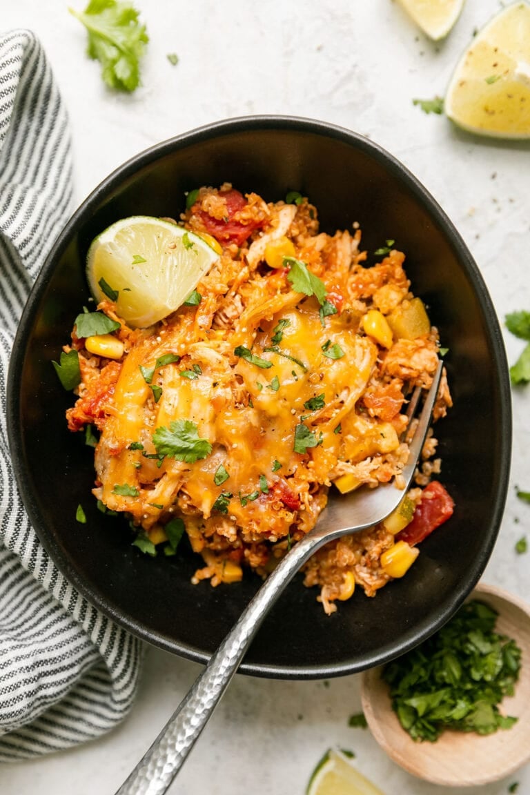 Overhead view of a plate filled with southwest quinoa chicken casserole topped with melted cheese and garnished with a lime wedge. 