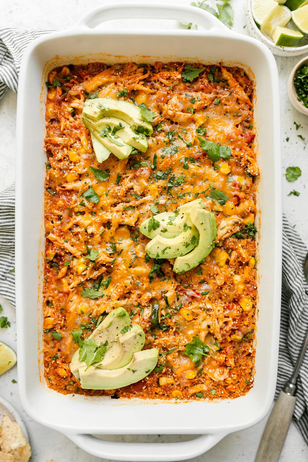 Overhead view chipotle quinoa casserole with chicken, topped with melted cheddar cheese and avocado slices. 