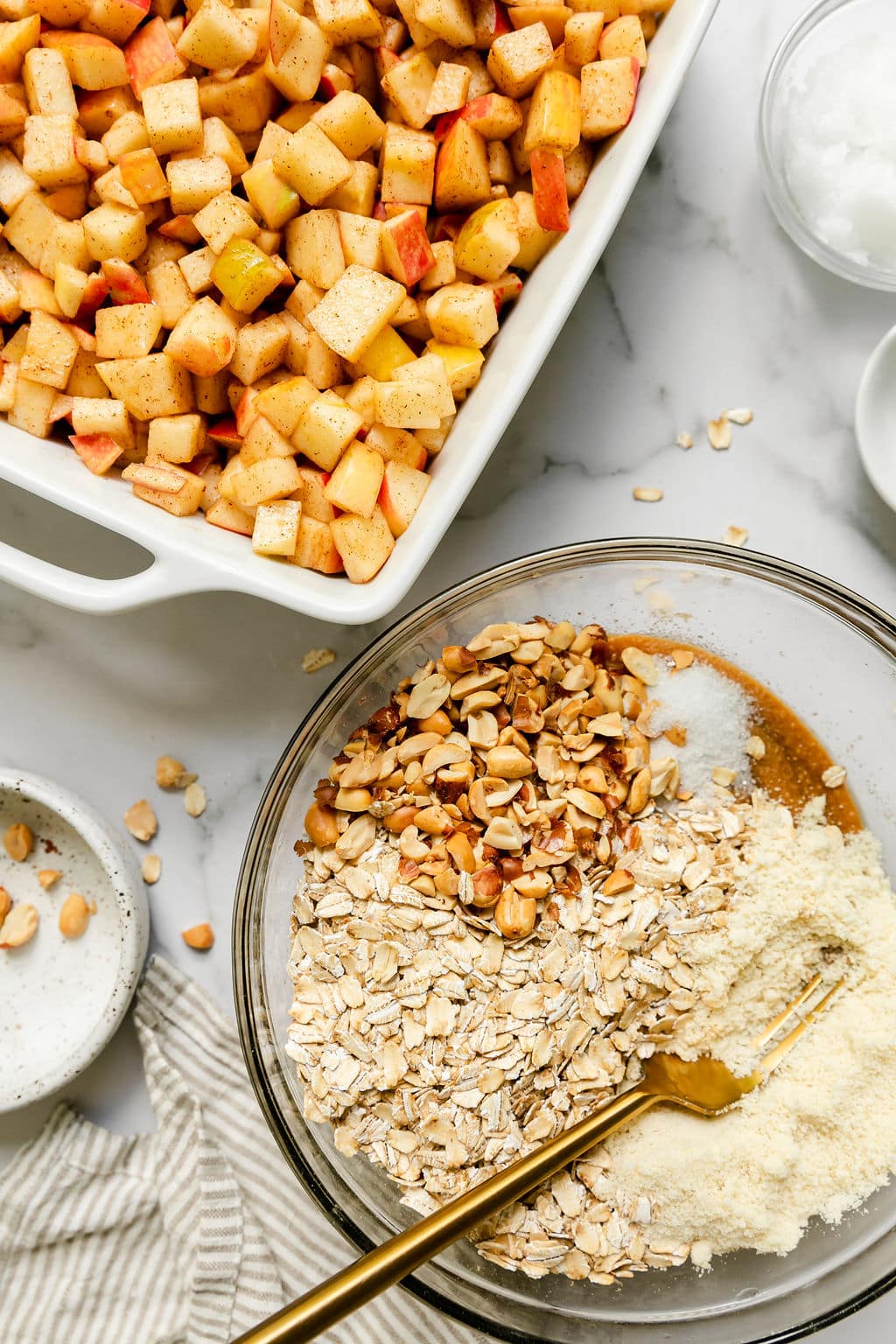 Close up view of a pan of diced apples and a bowl of topping ingredients for baking. 
