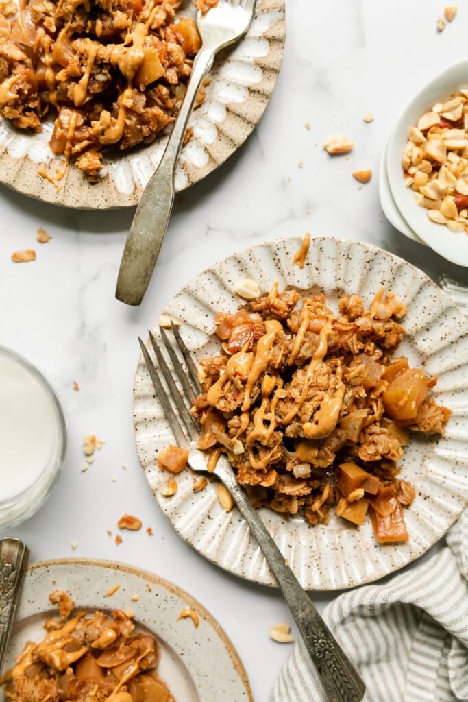 Two plates with servings of apple crumble with peanut butter oat crumble and peanut butter drizzled over top.