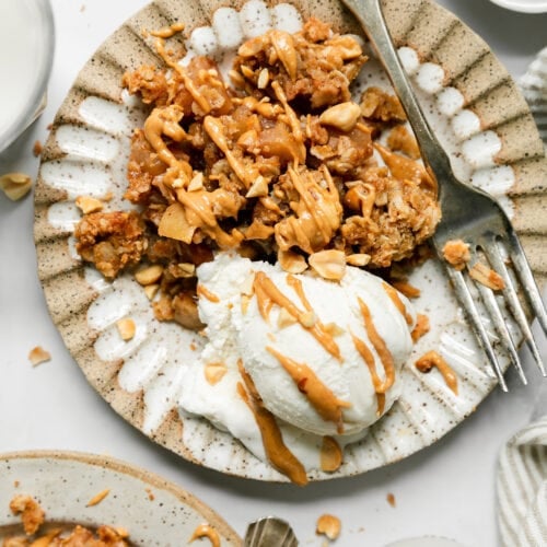A serving of peanut butter apple crisp on scalloped edge bowl with scoop of vanilla ice cream