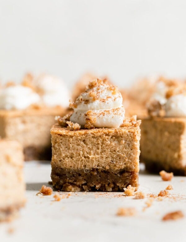 Side view single mini pumpkin cheesecake bar topped with dollop of whipped cream.