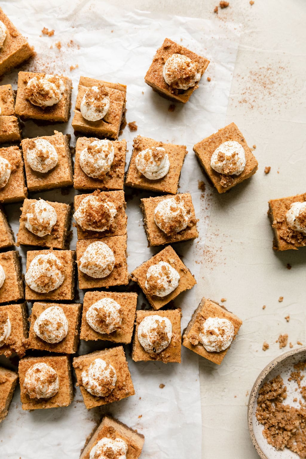 Overhead view several mini pumpkin cheesecake bars cut into small squares, each topped with dollop of whipped cream.