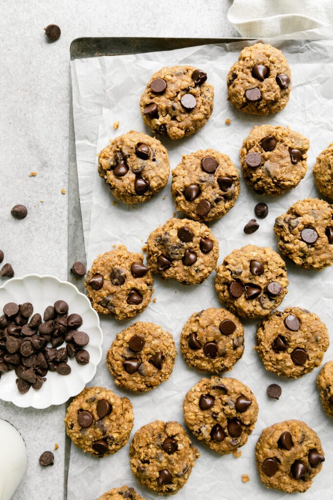 Oatmeal Pumpkin Chocolate Chip Cookies on a sheet pan with a dish of chocolate chips on the side
