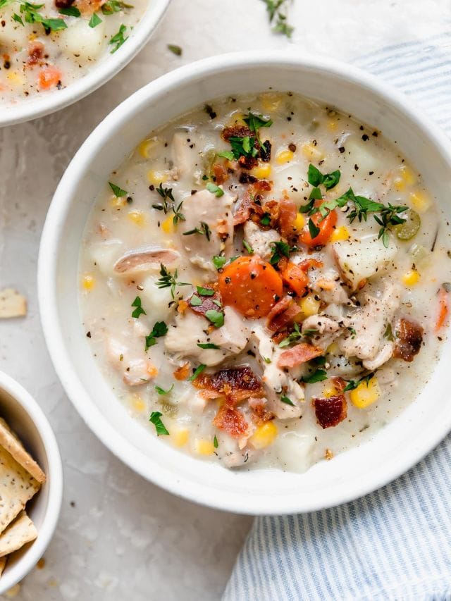Overhead view white bowl filled with slow cooker chicken corn chowder topped with fresh herbs and black pepper.