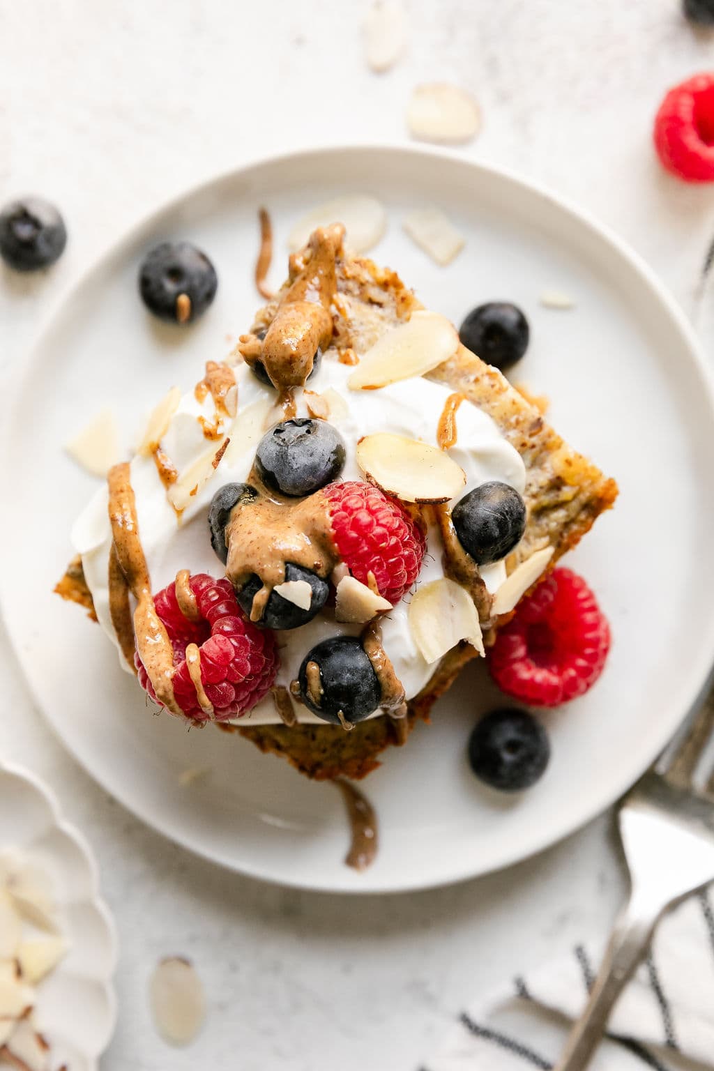 Overhead view serving of protein baked oatmeal topped with Greek yogurt, peanut butter drizzle and fresh raspberries and blueberries.