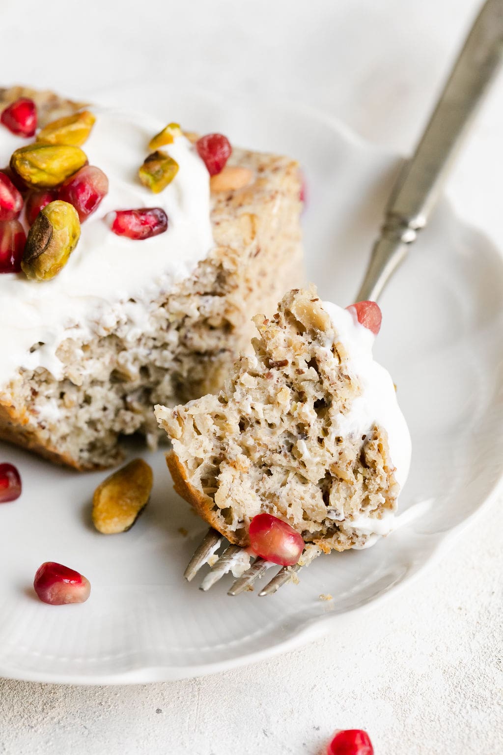 A bite of protein baked oatmeal on a fork with serving of baked oatmeal on a white plate. 