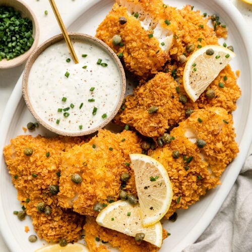 Overhead view white platter filled with baked cod fillets and small bowl of aioli sauce.