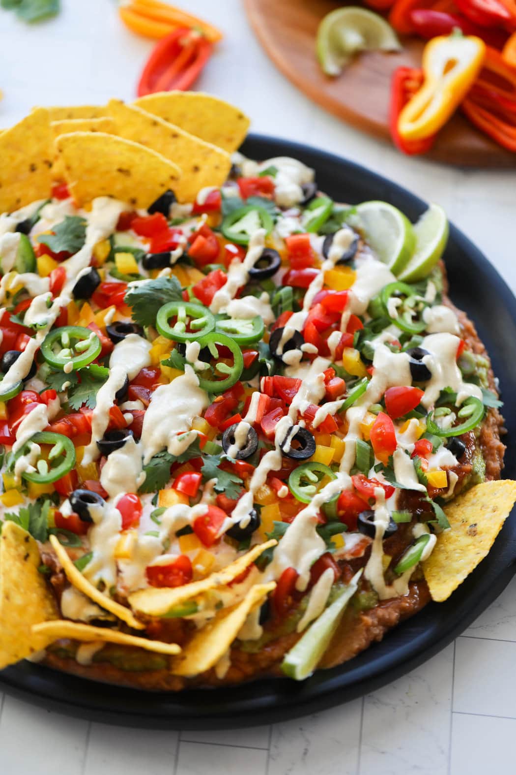 Black platter filled with 7 layer dip topped with fresh cut veggies, black olives, and plant based sour cream.