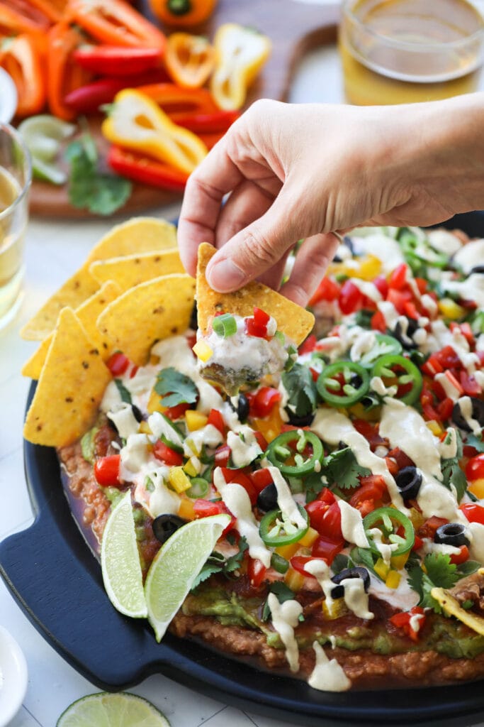 A corn tortilla scooping up a serving of 7 layer dip from a black platter.