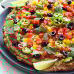 Side view black round tray with 7 layer dip spread and layered onto it. Topped with black olives, cut peppers, and lime wedges.