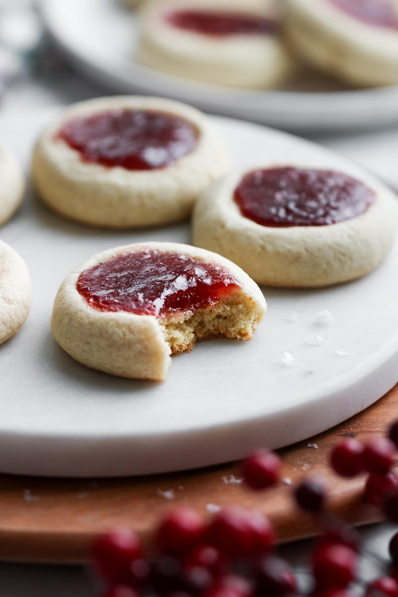Side view raspberry thumbprint cookies on white marble board, a bite taken out of nearest cookie.