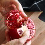Sections being removed from a whole pomegranate to remove pomegranate arils.