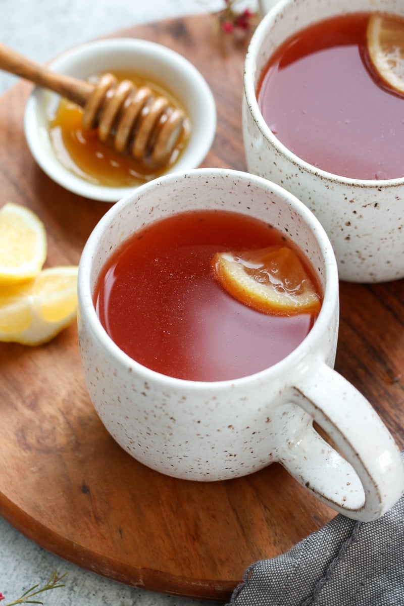Two mugs filled with homemade Starbucks Medicine Ball Tea on a round wooden tray.