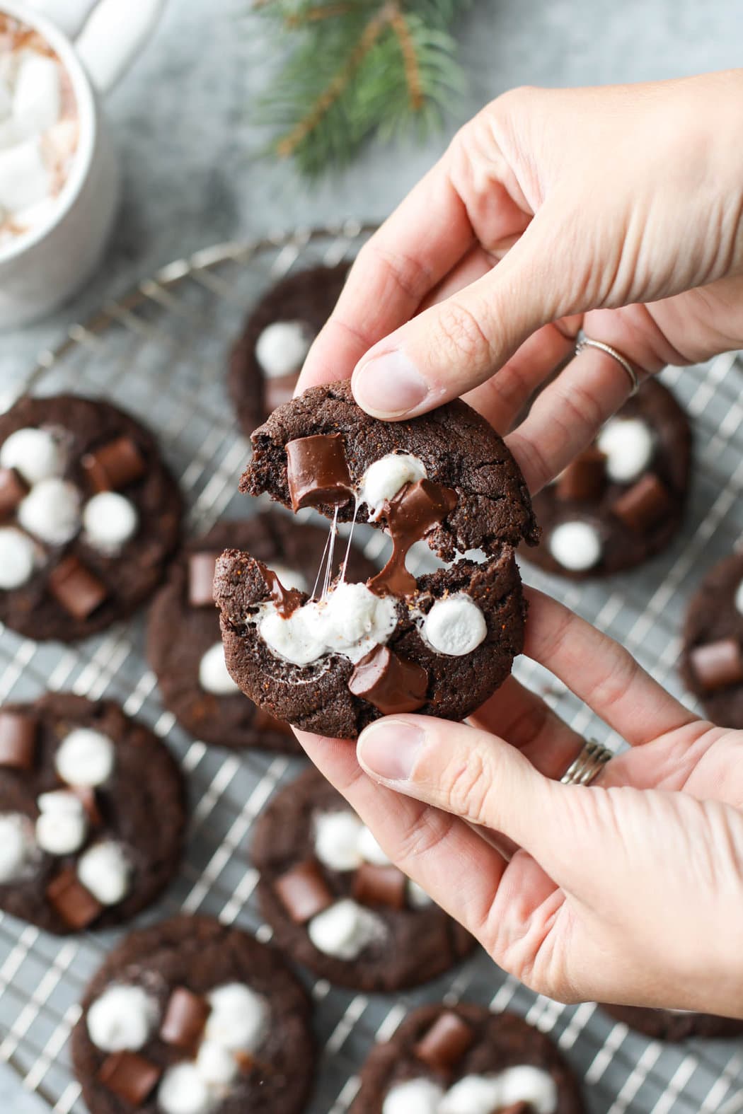 Two hands pulling apart a Mexican hot chocolate cookie with melty marshmallow strings between the cookie halves.