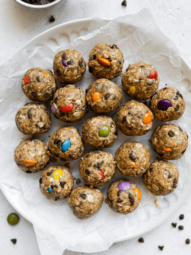 Overhead view several monster cookie protein balls with colorful candy pieces in each ball on a parchment-covered white platter.
