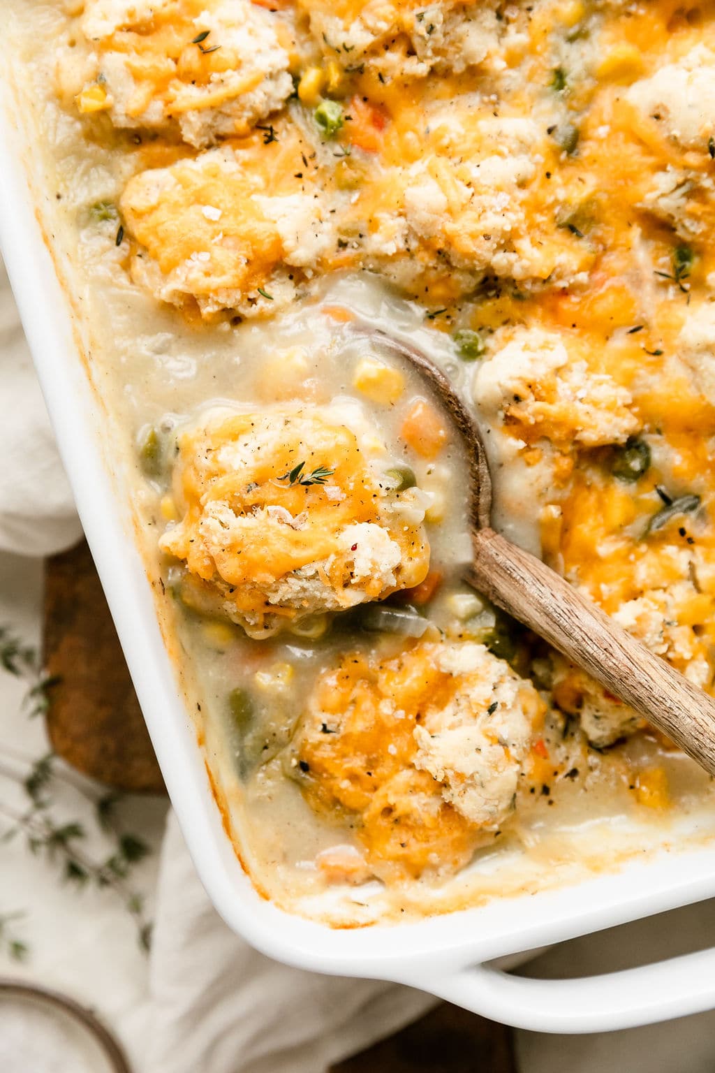 Overhead view bubbly chicken pot pie casserole in white casserole dish with wooden serving spoon scooping up portion.