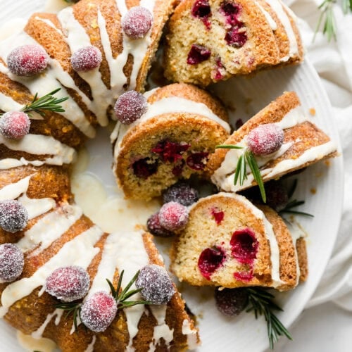 Cranberry orange olive oil bundt cake on white platter, several slices cut and turned sideways to show texture.