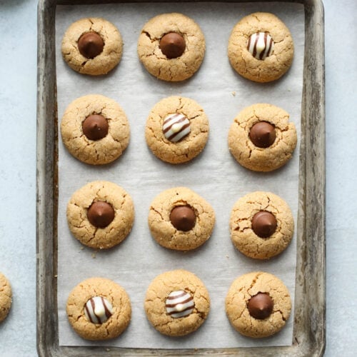 Peanut butter blossoms lined up on parchment covered baking sheet.