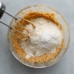 Overhead view hand mixer in bowl filled with ingredients for peanut butter blossoms ready to be mixed together.
