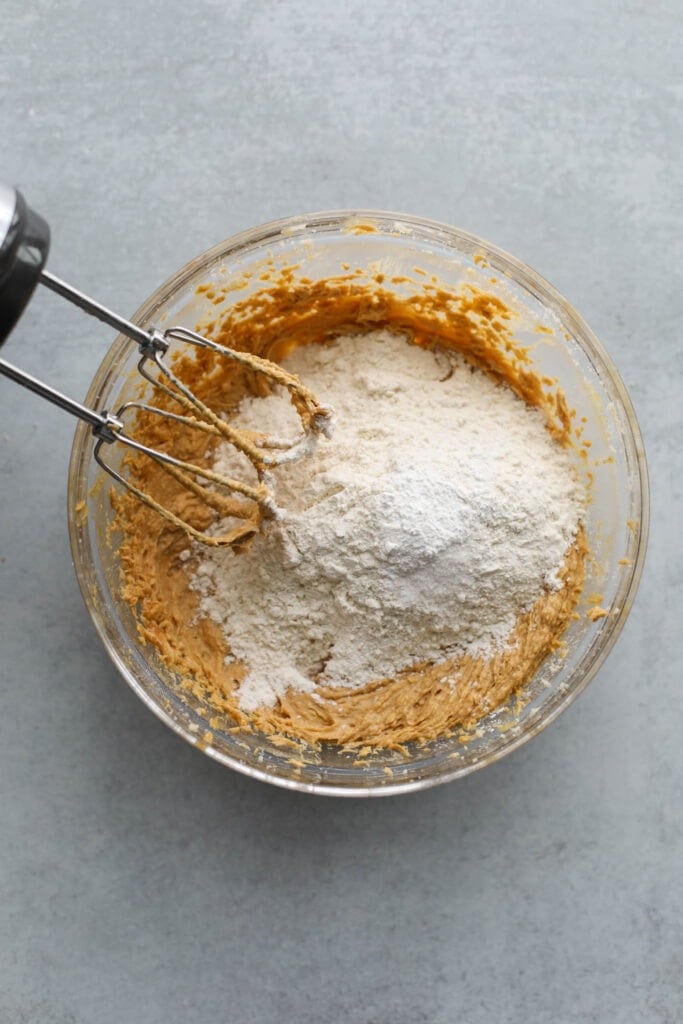 Peanut butter blossoms dough in mixing bowl with dry ingredients on top ready to mix in.