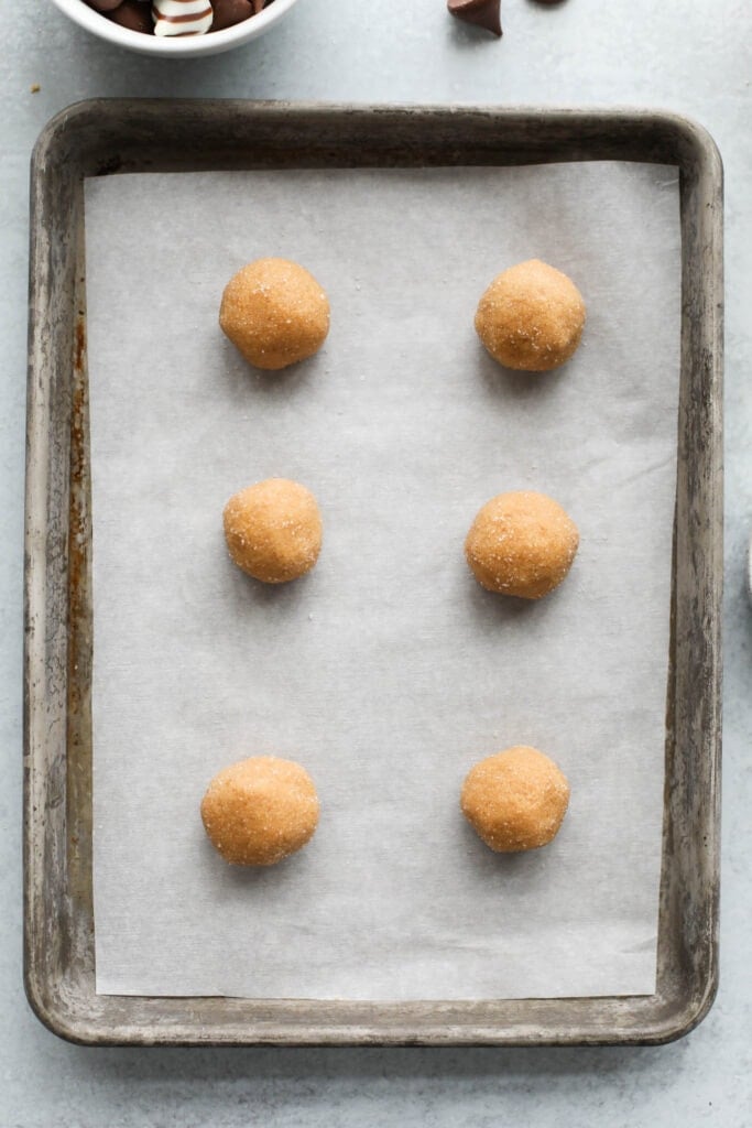 Peanut butter blossoms dough balls lined up on parchment covered baking sheet.