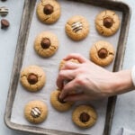 A chocolate kiss being pressed into a warm peanut butter blossom cookies on a baking sheet.