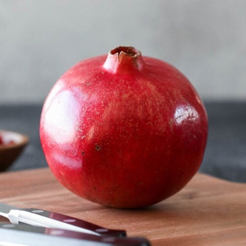 A single fresh pomegranate on a wooden cutting board.
