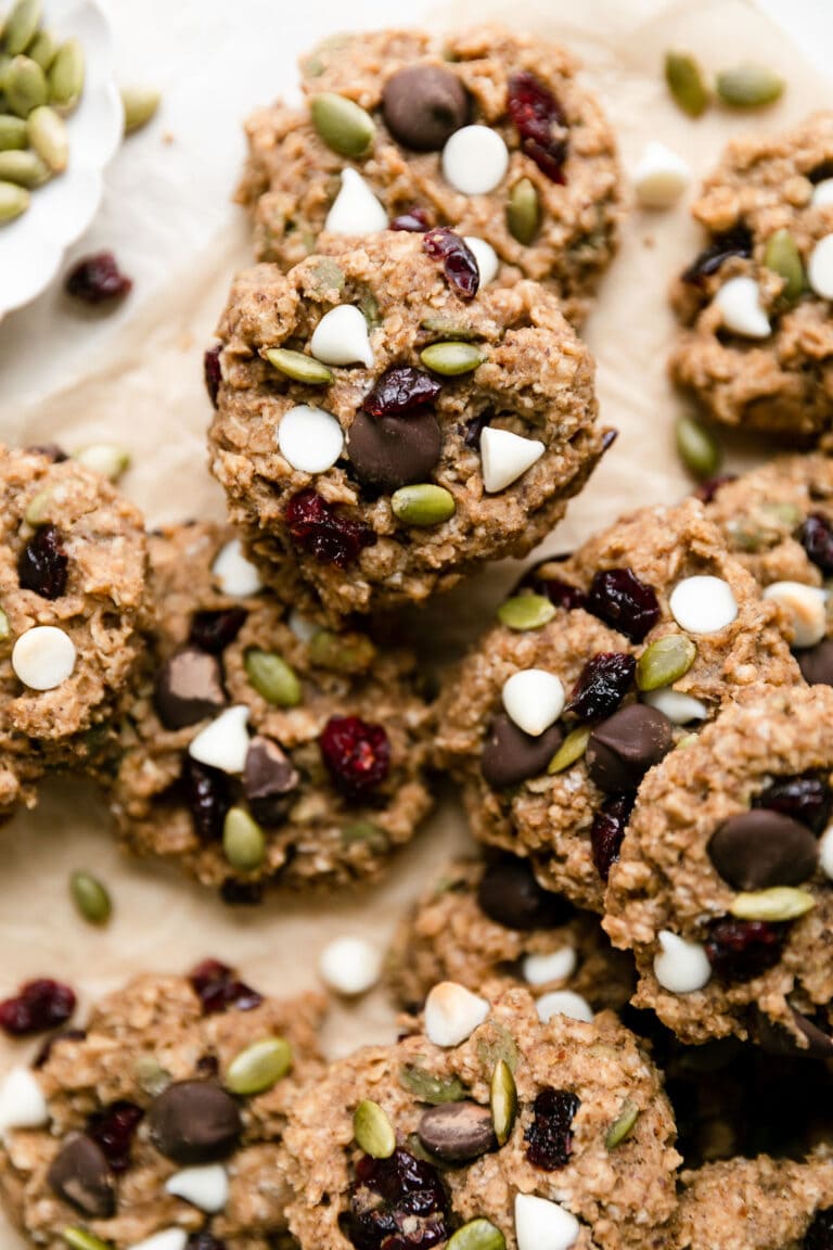 Overhead view of a pile of trail mix breakfast cookies on parchment paper studded with white chocolate chips and pepitas.