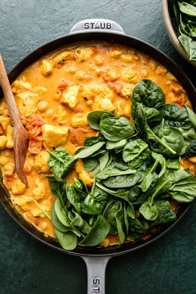 Process shot, cast iron skillet filled with chicken curry with chickpeas and spinach