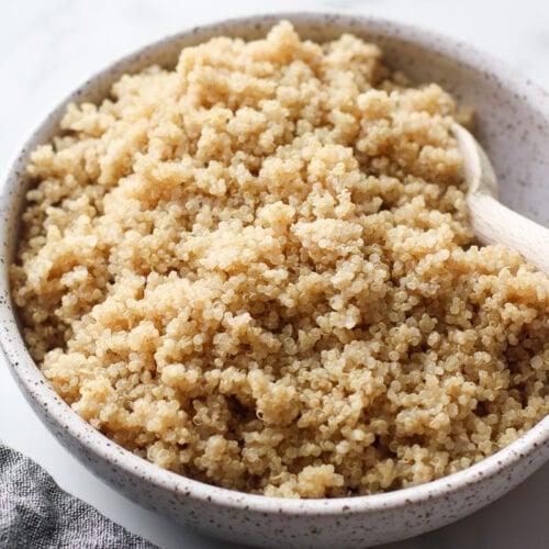 A stone bowl filled with cooked quinoa, wooden spoon in quinoa