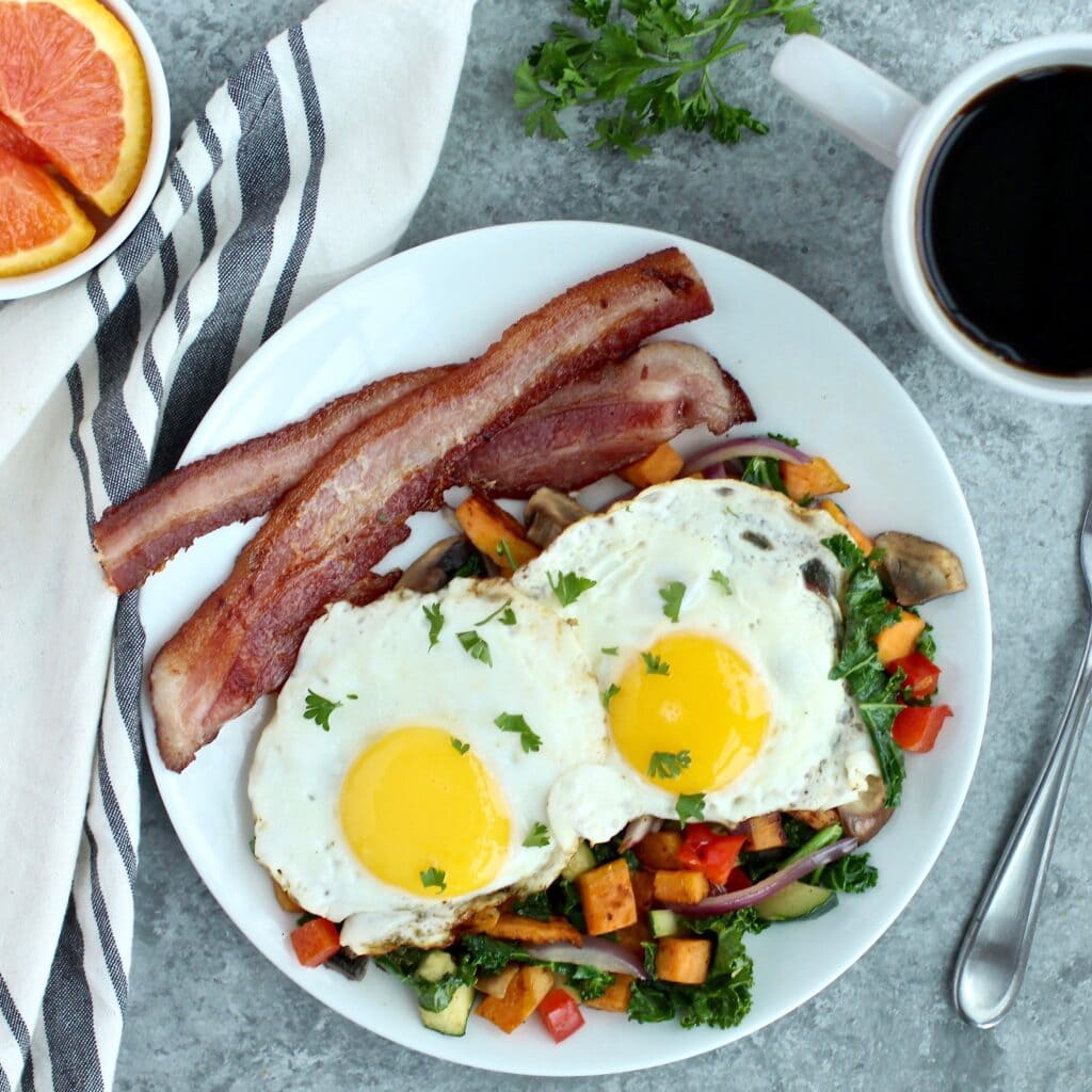 Overhead view of a plate of fried eggs over vegetables and two pieces of bacon. 