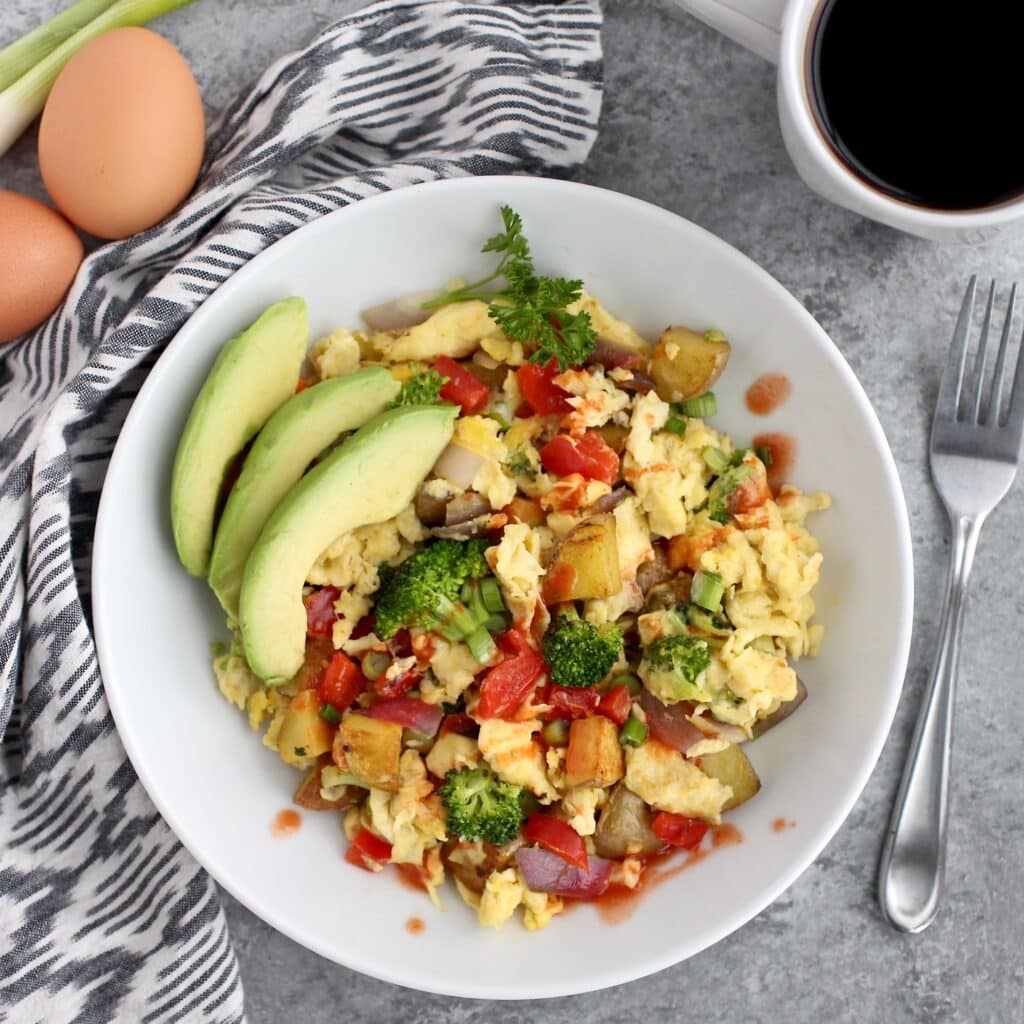Overhead view of a plate of a vegetable scramble with sliced avocado on the side. 