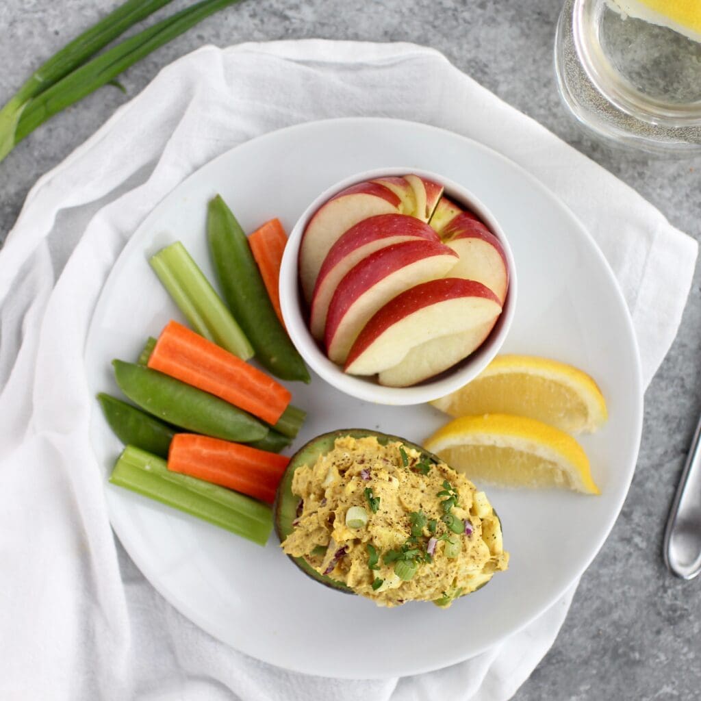 Overhead view of a plate of curried tuna salad stuffed avocado and fruit. 
