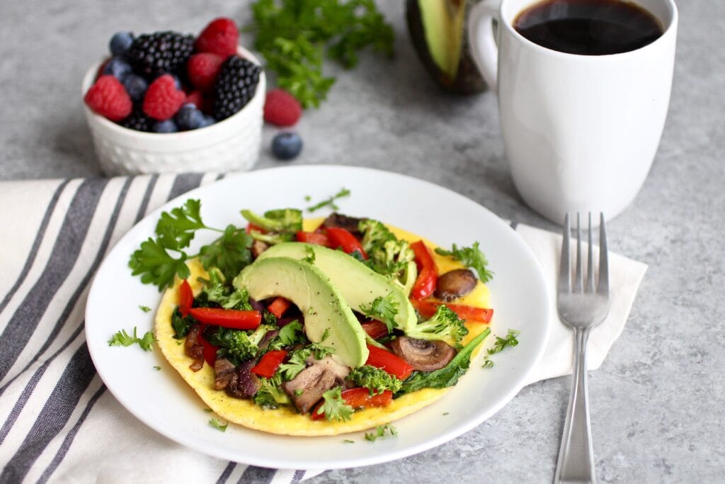A place setting including a cup of coffee, berries, and a plate filled with a vegetable omelet topped with avocado and cilantro. 