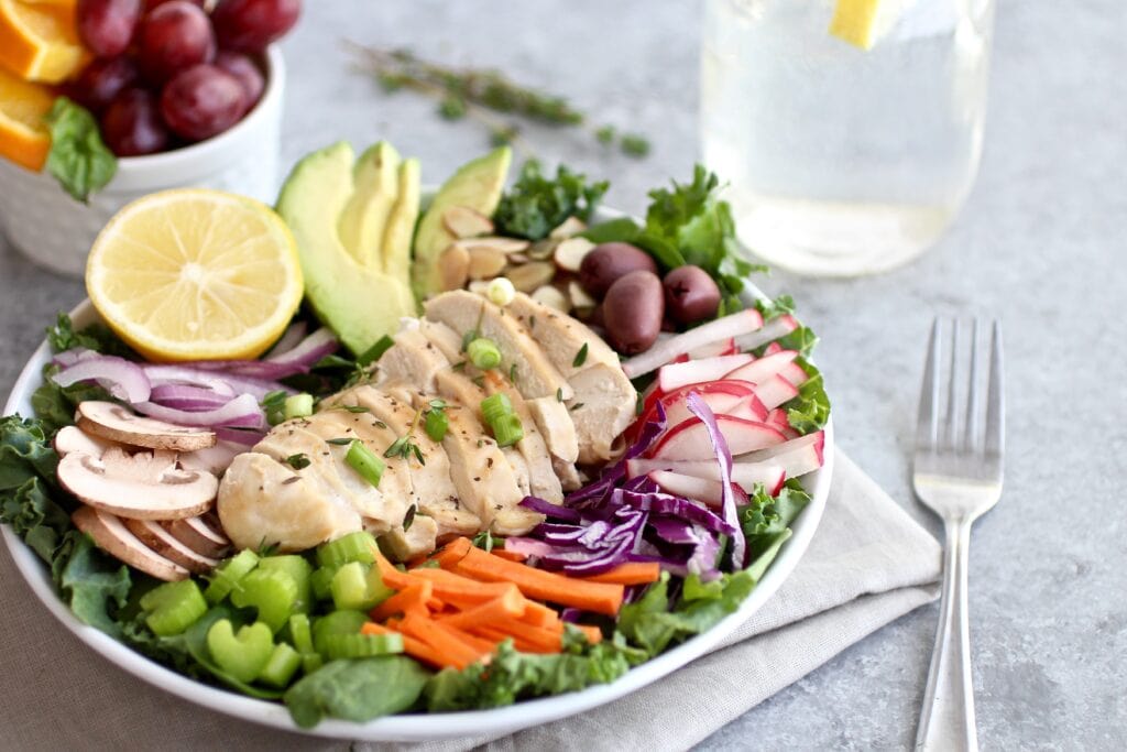 Close up view of a white plate filled with a salad topped with chopped vegetables and sliced chicken breast.