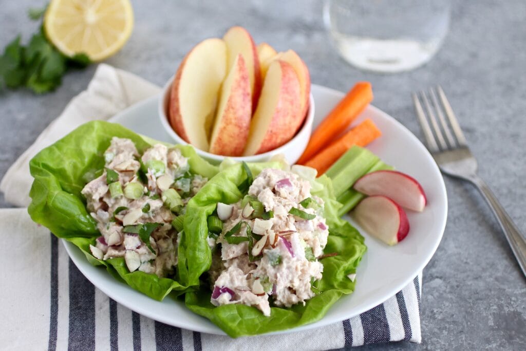Close up view of a plate of lettuce wraps with sliced apples and carrot sticks on the side. 