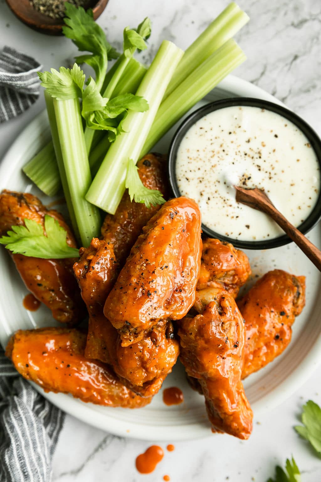 Overhead view white platter filled with buffalo chicken wings, celery sticks and black bowl filled with ranch dressing.