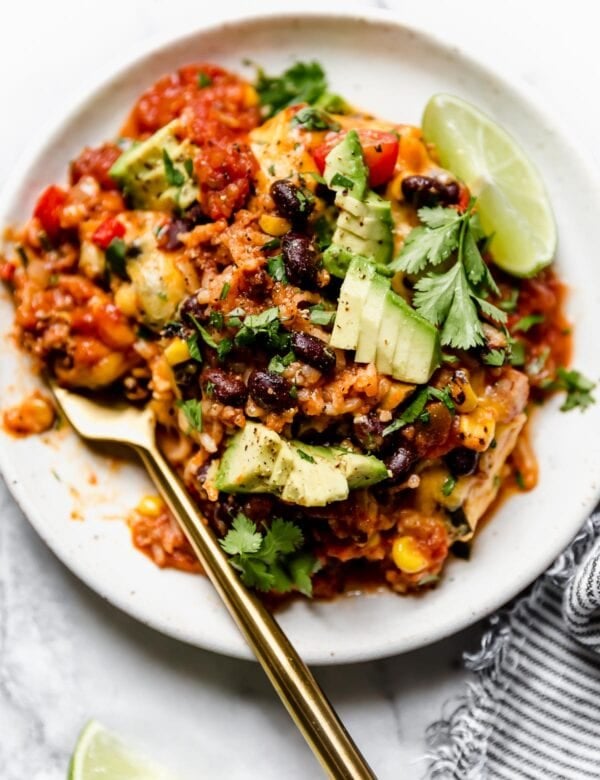 A round plate with a serving of taco casserole topped with diced avocado and lime slices