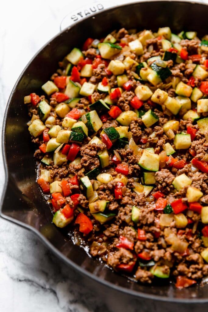 Taco meat with diced zucchini and red bell pepper in cast iron skillet.