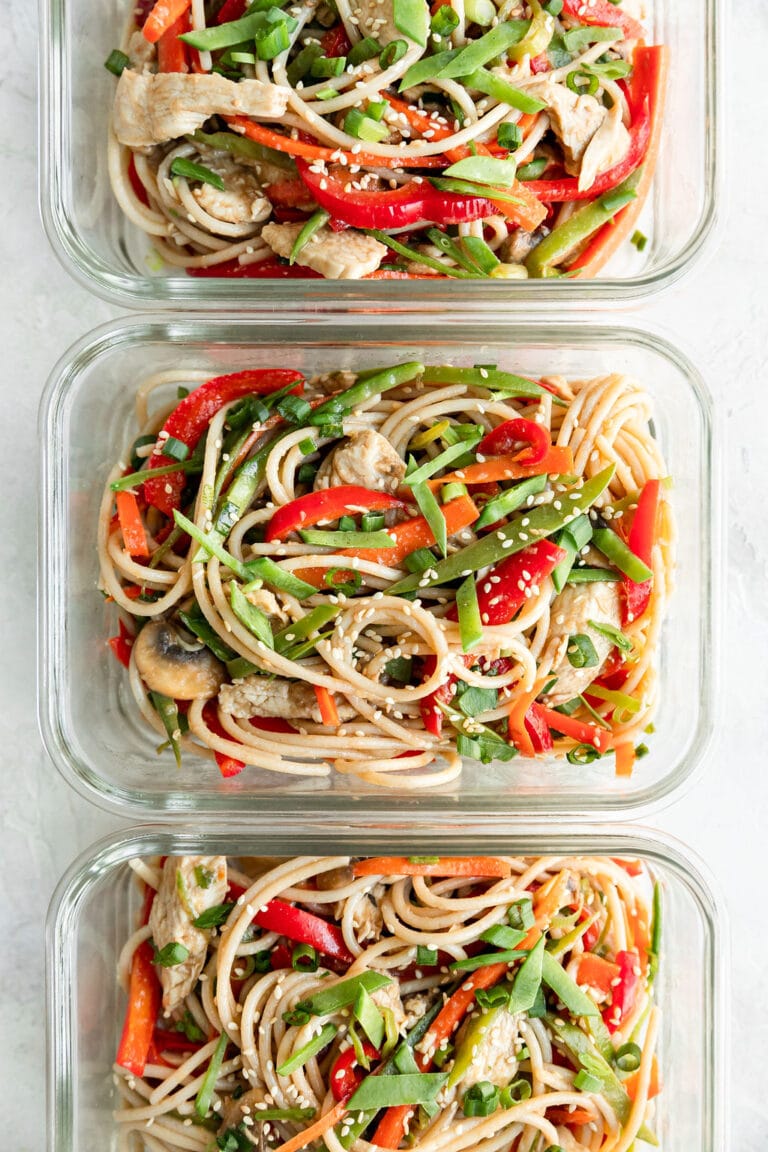 Overhead view of three glass meal prep containers filled with stir fry noodles with chicken topped with sesame seeds.