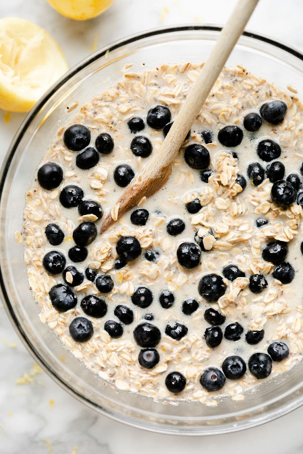 Close up view of a bowl of oatmeal with a wooden spoon stirring in fresh blueberries.