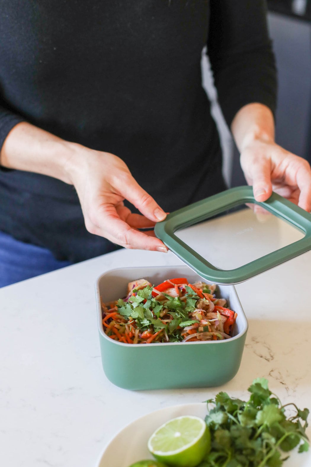 A meal prep storage lid being placed on a container filled with fresh pad thai.