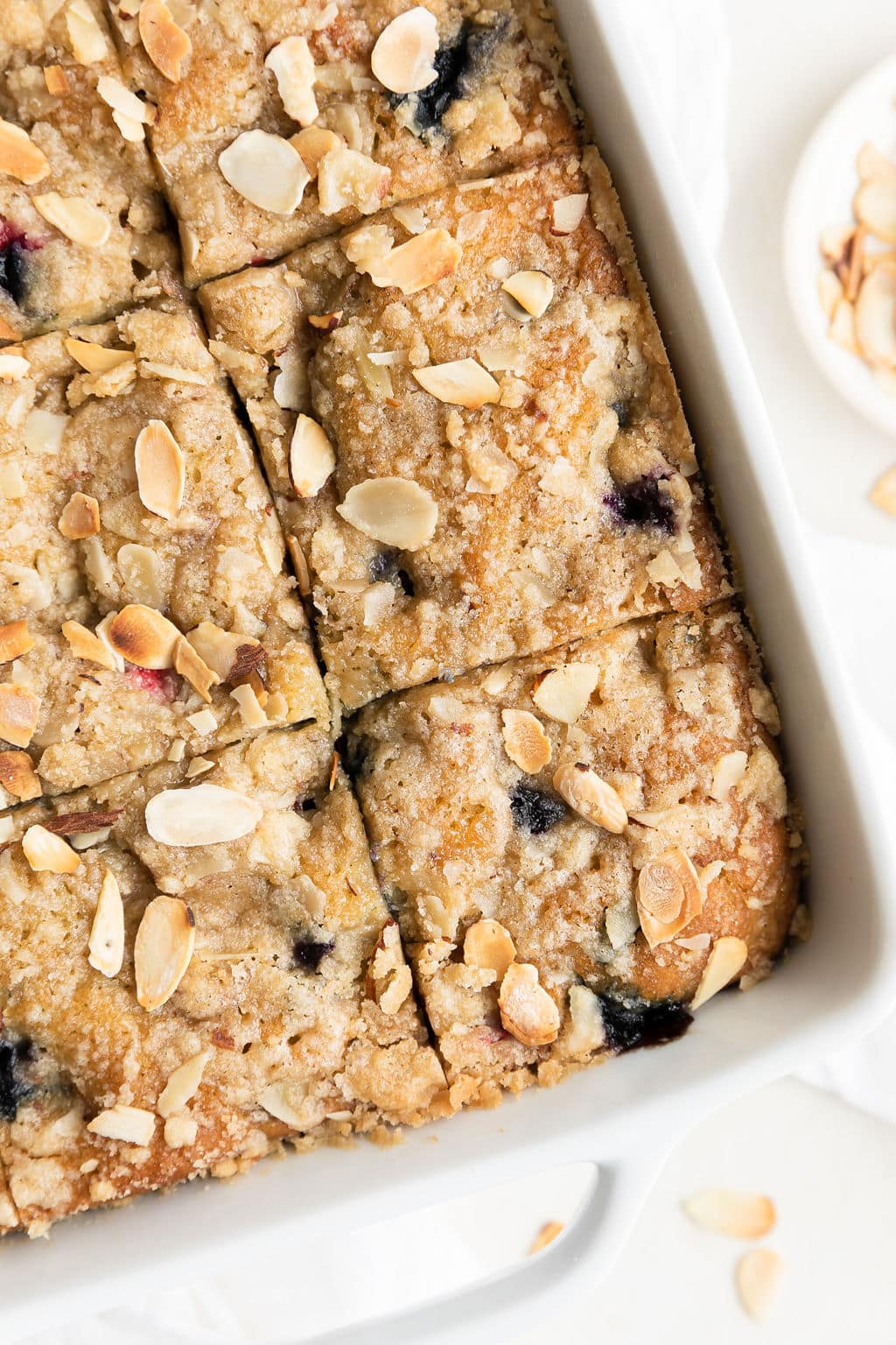 Close up view mixed berry breakfast cake in white baking dish cut into squares.