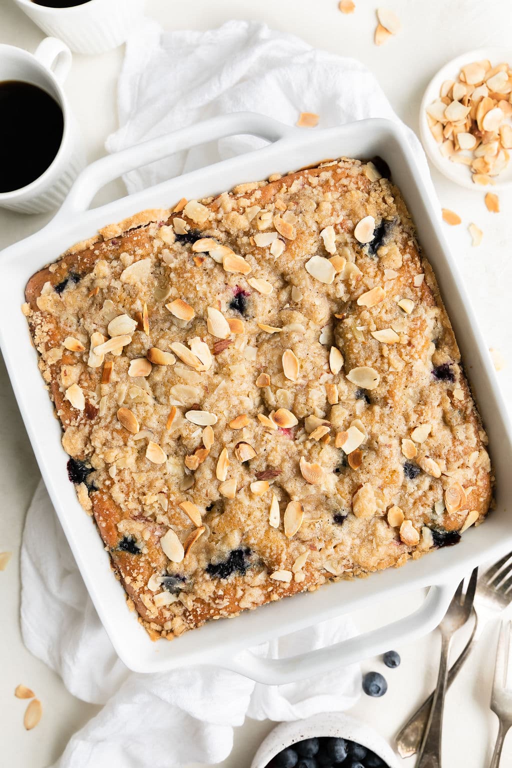 Overhead view white baking dish with baked mixed berry breakfast cake with crumb topping and sliced almonds. 