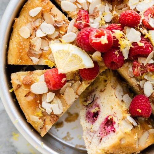 Raspberry lemon coffee cake in round pan, cut into slices, one slice on side to show inside texture.